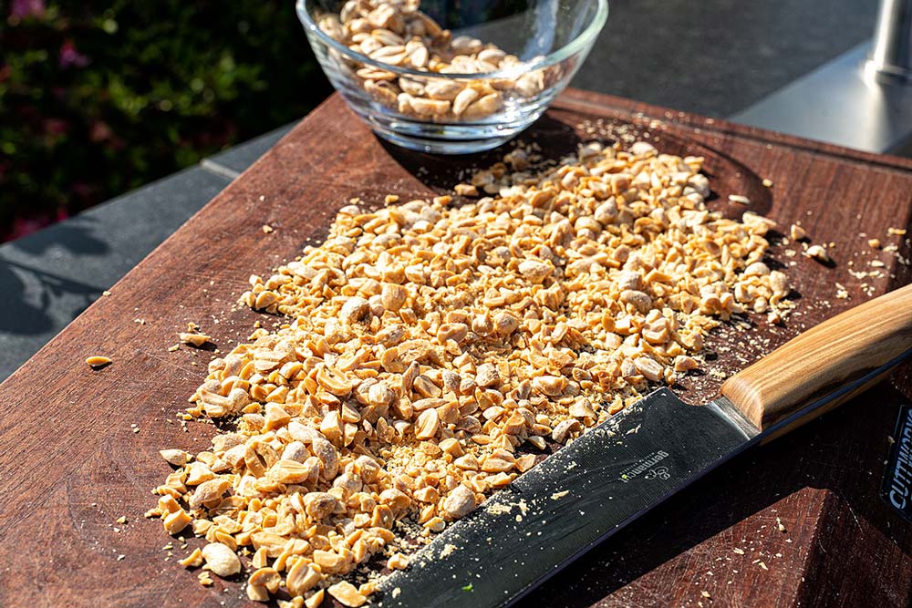 Für den Erdnussmantel hacken wir die Erdnüsse grob und verteilen diese auf einem flachen Brett.