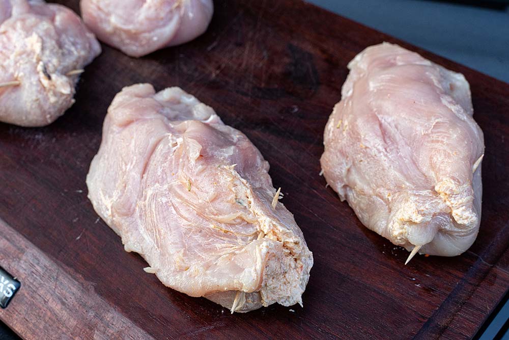 Die Füllung geben wir nun in die zuvor geschnittenen Tasche in den Hähnchenbrüsten. Die Öffnung verschließen wir mit einem Zahnstocher oder einer Rouladennadel.