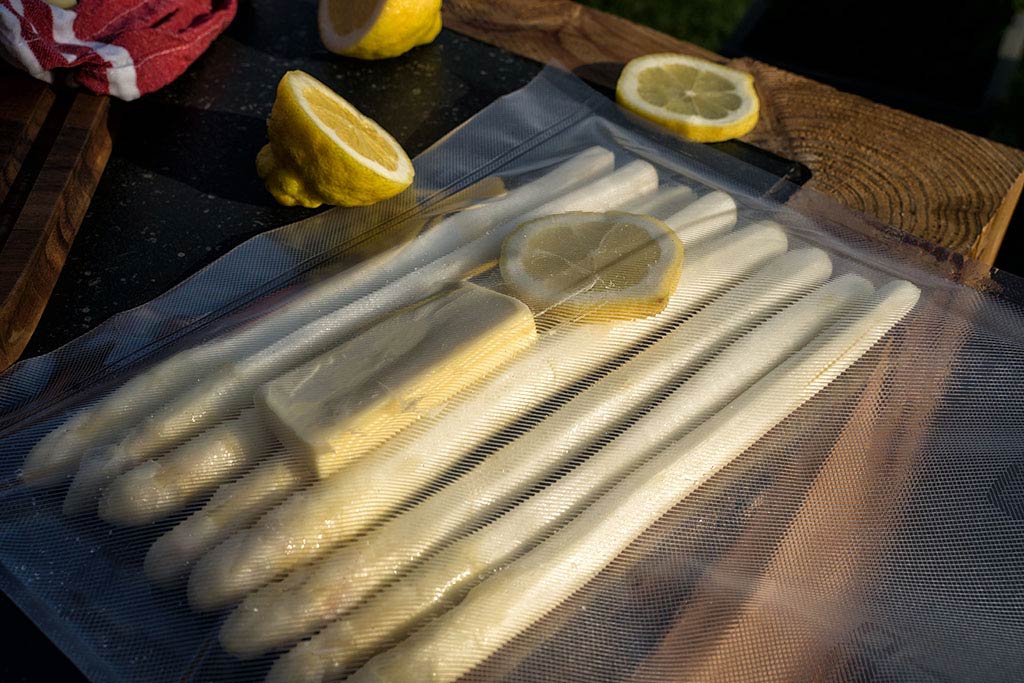 In zwei Vakuumbeuteln jeweils 8 Stangen Spargel mit einem halben TL Salz, 
             einem halben TL Zucker, zwei EL Butter und einer Scheibe Zitrone einschweißen.