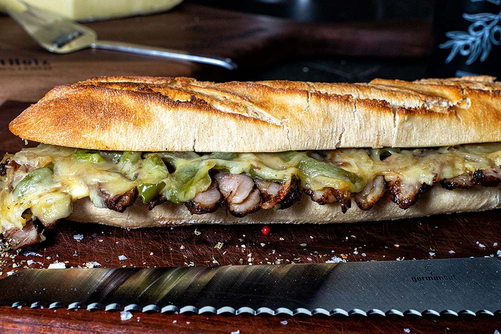 Wir stülpen die Grillschale um, sodass der Sandwichdeckel unten und das Steak oben ist. Nun salzen und pfeffern wir das Steak, legen das Unterteil des Baguettes auf und drehen das Baguette wieder um.