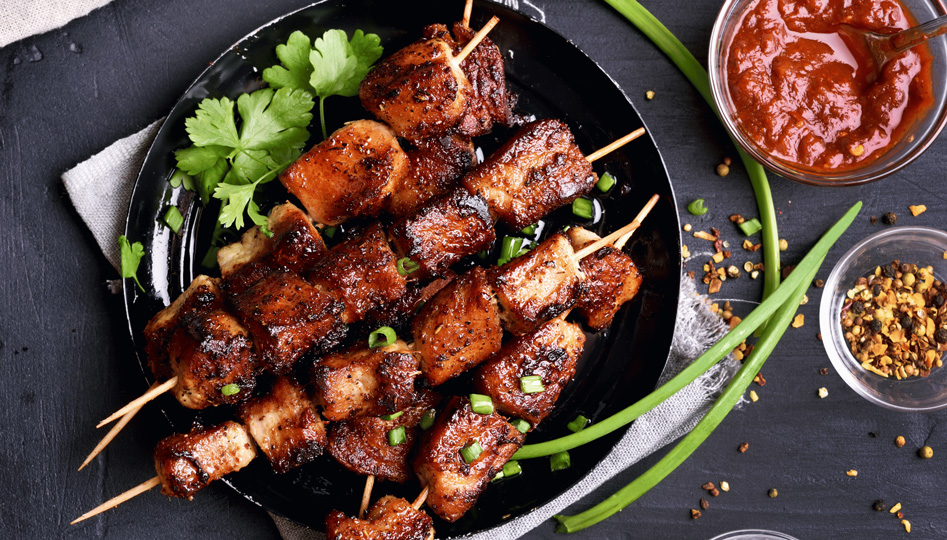 Tipps zum Grillen Titelbild. Ein Teller mit gegrilltem Fleisch, daneben Ketchup in einer Glasschale, Gewürze und Kräuter als Dekoration 