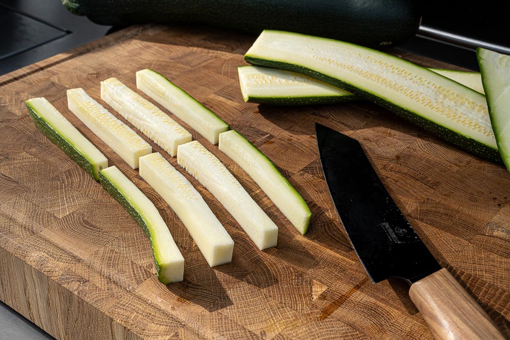 Die Zucchini längs in ca. 1,5 cm breite Scheiben und anschließend jeweils 
                     in 4 Stifte schneiden und anschließend in der Mitte teilen.