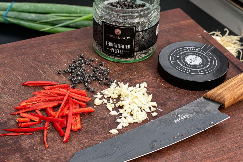 Die beiden Knoblauchzehen und den Ingwer klein hacken, die Chili in Streifen schneiden und anschließend zusammen mit dem fermentierten Pfeffer vermischen.