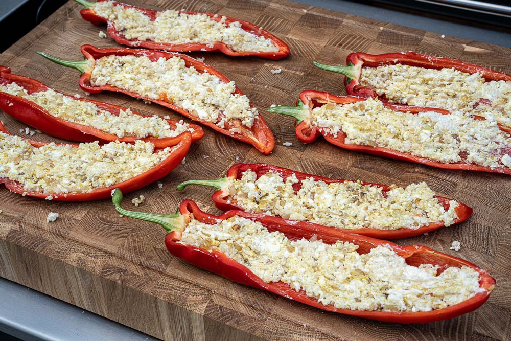 Die angeschwitzten Zwiebeln mit dem Frischkäse, dem Feta und dem 
                    Couscous verrühren, anschließend mit Curry, 
                    feinem Meersalz und gutem Pfeffer würzen. Im Anschluss 
                    die Häften gleichmäßig mit der Masse füllen.