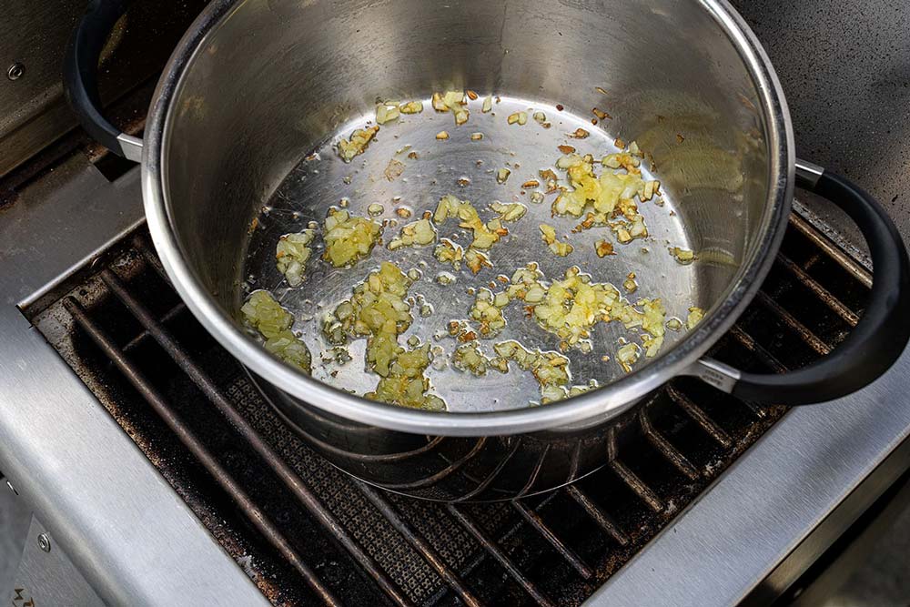 In einem mit Olivenöl benetztem Topf schwitzen wir den Knoblauch und die Zwiebeln auf unserem Burner an.