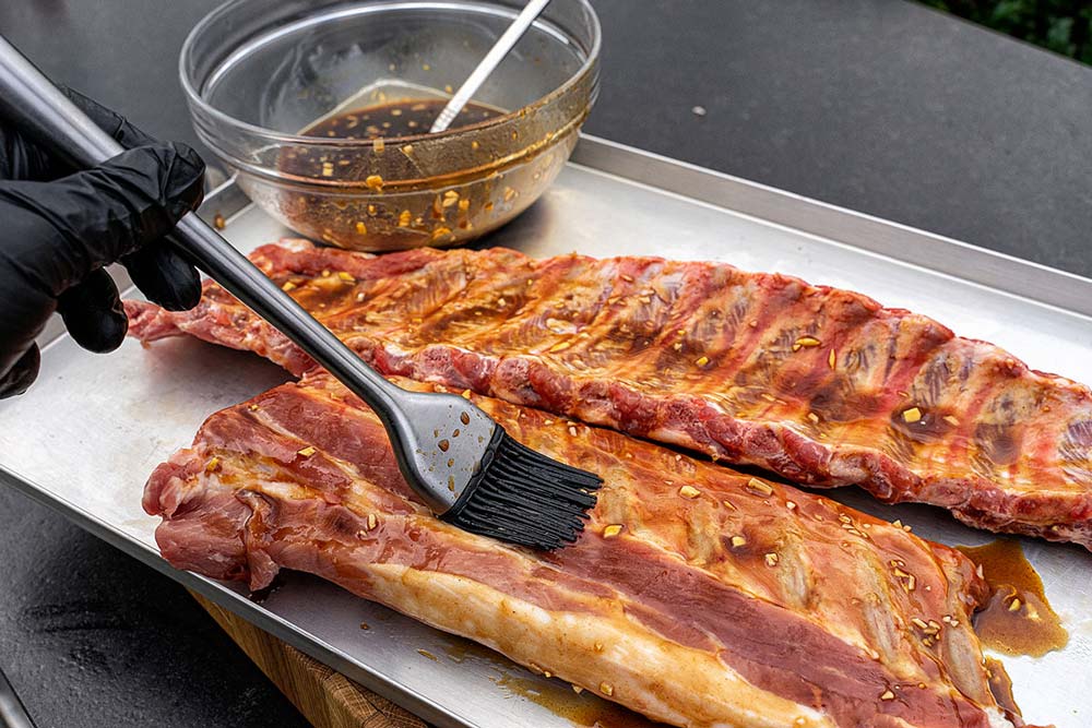 Die Silberhaut der Spare Ribs entfernen, mehrmals großzügig mit der Asia Marinade bestreichen und anschließend idealerweise für mindestens 2 Stunden im Kühlschrank einwirken lassen.