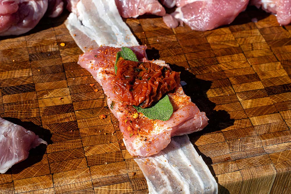 Auf das gewürzte Stück Kachelfleisch geben wir ein Blatt Salbei und eine getrocknete Tomate.