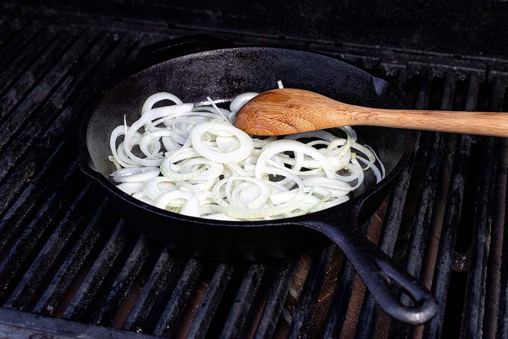 Sobald die Gusspfanne aufgeheizt ist, geben wir ein bisschen Olivenöl hinein und dünsten die Zwiebeln an.