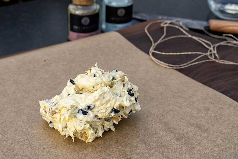 Die geachtelten Oliven unter die Butter heben, 
                    mit Pfeffer und Meersalz würzen und anschließend auf Backpapier legen.