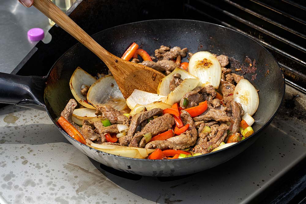 Asiatische Gerichte gelibgen spielend mit dem Wok und der Auflage L