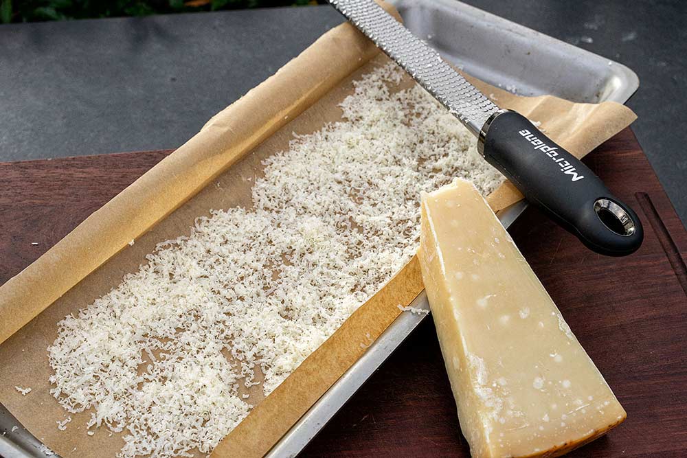 Parmesan raspeln und auf mit Backpapier ausgelegte Grillschale streuen.